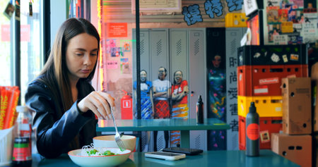 Fashionable woman savoring a flavorful ramen dish in a vibrant and stylish restaurant, capturing the essence of modern dining and culinary enjoymentの写真素材
