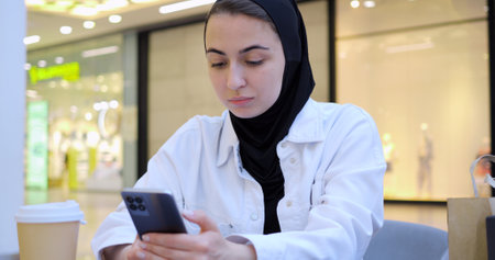 Young woman engaging with smartphone while enjoying coffee in trendy cafe, embodying modern digital connectivity and leisurely urban lifestyle during focused moment of communicationの写真素材