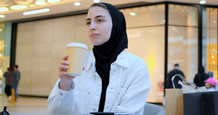 Young woman engaging with smartphone while enjoying coffee in trendy cafe, embodying modern digital connectivity and leisurely urban lifestyle during focused moment of communicationの写真素材