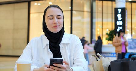 Young woman engaging with smartphone while enjoying coffee in trendy cafe, embodying modern digital connectivity and leisurely urban lifestyle during focused moment of communicationの写真素材