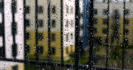 Close view of raindrops clinging to window glass with out of focus colorful facades of residential...