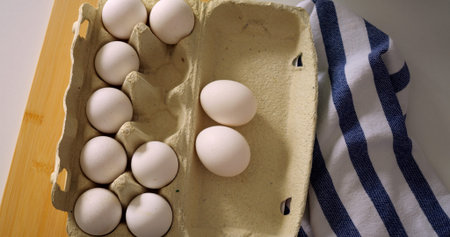 Two raw eggs being whisked with fork, hand holding utensil on wooden table with striped towel,...