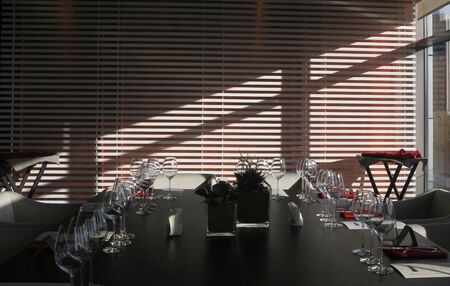 Sun light illuminates a wooden table full of empty glasses and white candlesの写真素材