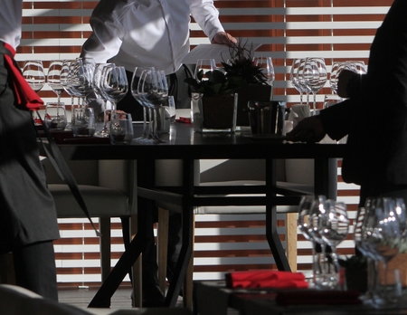 Sun light illuminates a wooden table full of empty glasses and white candlesの写真素材