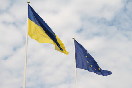 Flags of European Union and Ukraine waving on flagpoles isolated on white background.