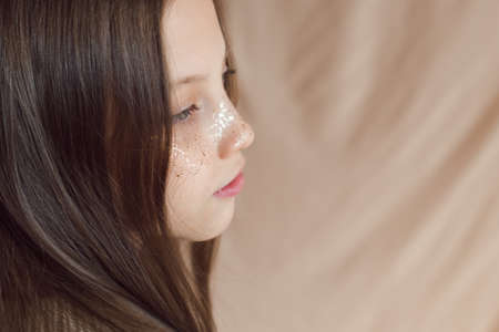 beautiful teenage girl with golden freckles on face posing on beige backgroundの写真素材