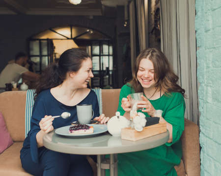 two women talking and drinking coffee in cafeの写真素材