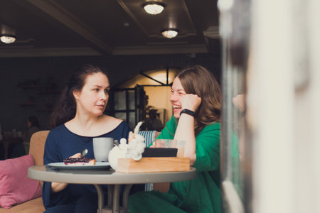 two women talking and drinking coffee in cafeの写真素材