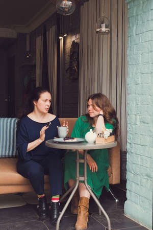 two women talking and drinking coffee in cafeの写真素材
