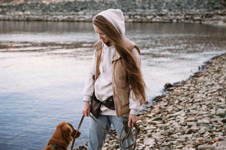 young woman and dog retriever walks on river shore at autumn seasonの写真素材