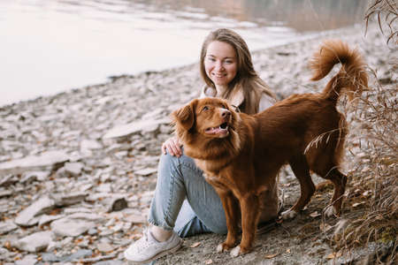 young woman and dog retriever walks on river shore at autumn seasonの写真素材