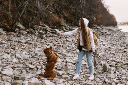 young woman and dog retriever walks on river shore at autumn seasonの写真素材