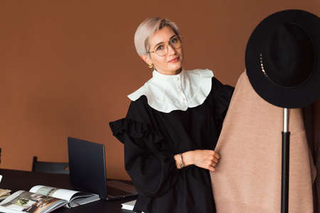 fashion woman in vintage black and white dress standing in modern work place or office at hangers with clothesの写真素材