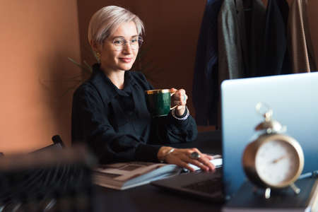 fashion woman in black shirt working in modern work place or office with laptop and coffe cupの写真素材