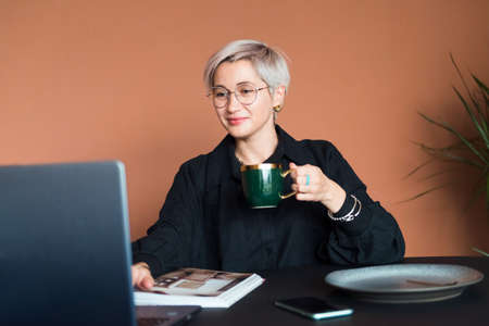 fashion woman in black shirt working in modern work place or office with laptop and coffe cupの写真素材
