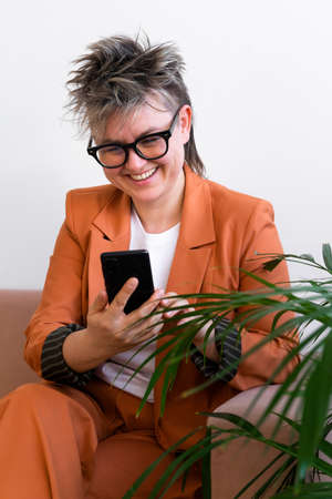 fashion business woman queer portrait, sitting on couch, using social mediaの写真素材