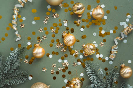 new year decorations golden color with confetti and fir branches on color backgroundの写真素材