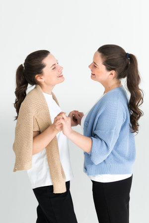 Two beautiful women twin sisters posing white background, having fun together
