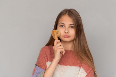 Cute teenage girl posing with face skin care brush, self-care routine
