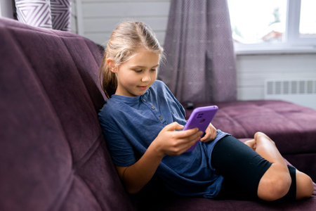 child sitting on sofa at home using smartphoneの写真素材