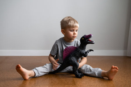 portrait of boy playing big dinosaur toy sitting on floorの写真素材