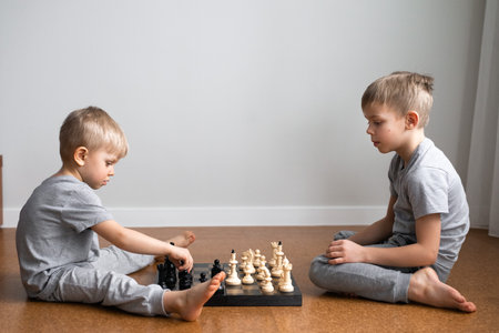 two boys brothers playing chess, sitting on floor at homeの写真素材