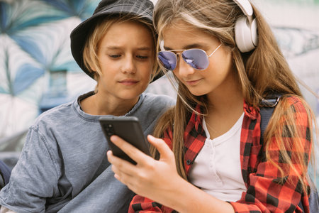 teenage boy and girl outdoors portrait, communicating and looking at smartphoneの写真素材