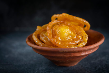 Jalebi fried indian crispy sweet dish in clay vessel on dark