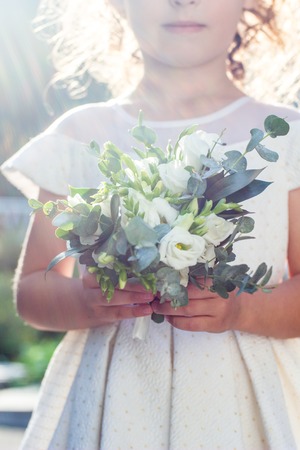White wedding bouquet holding by white dressed baby girl outdoorsの写真素材