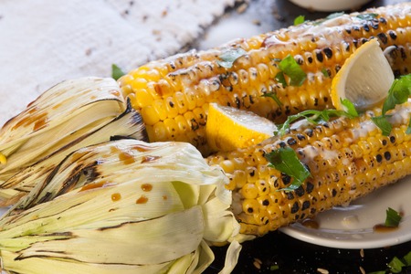 grilled corn on a wooden plate with lemon, herbs and spicesの写真素材