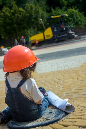 Little baby girl builder with the construction helmet and poster in denim uniform smiling on construction siteの写真素材