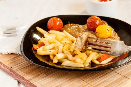 Vegetarian steak made from vegan meat - seitan, with cherry tomatoes and fries on black plateの写真素材