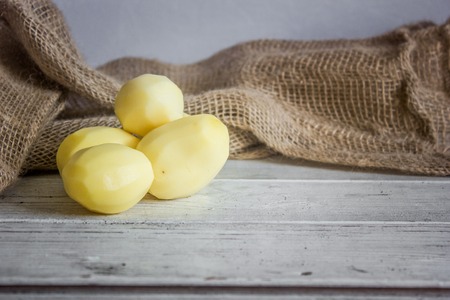 Group of peeled potatoes on white wooden table.の写真素材
