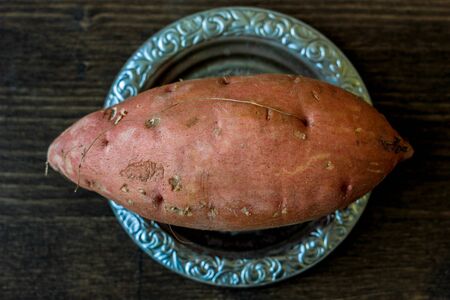 Raw sweet potatoes on metal plate over wooden tableの写真素材