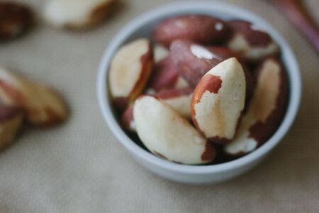 Heap of brazil nuts in white ceramic bowl over the brown fabricの写真素材