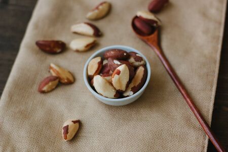 Brazil nuts in white ceramic bowl on brown fabric.の写真素材
