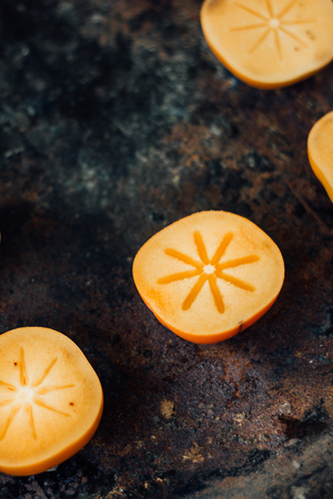 Halves of persimmon fruit on black metal surfaceの写真素材