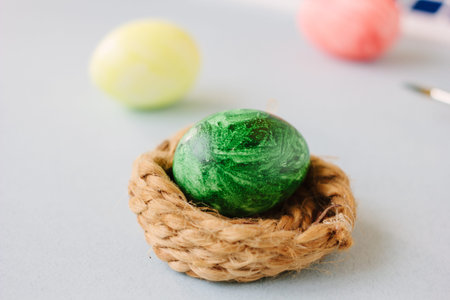 Green color easter egg in small nest over bright background.