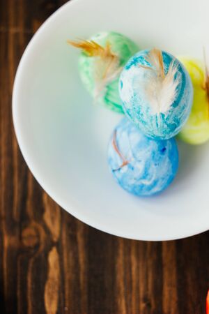 Blue, yellow and green color easter eggs on ceramic bowl over rustic tableの写真素材
