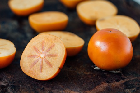 Halves of persimmon fruit on black metal surfaceの写真素材
