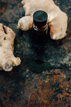 Ginger essential oil in glass bottle with ginger root behindの写真素材