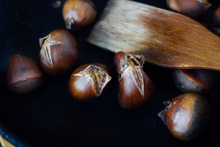 Roated chestnuts on cast-iron pan over wooden surface.の写真素材
