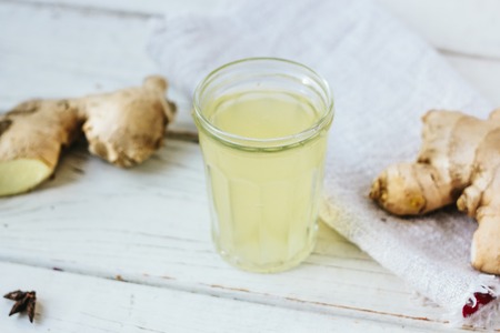 ginger juice in small glass jar with ginger root behindの写真素材