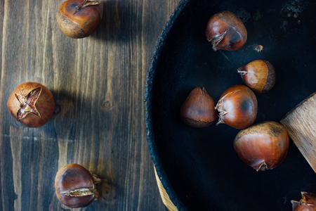 Roated chestnuts on cast-iron pan over wooden surface.の写真素材