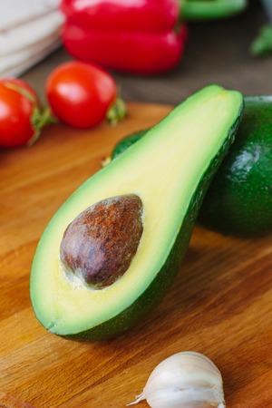 Avocado fruit on wooden board with other vegetablesの写真素材