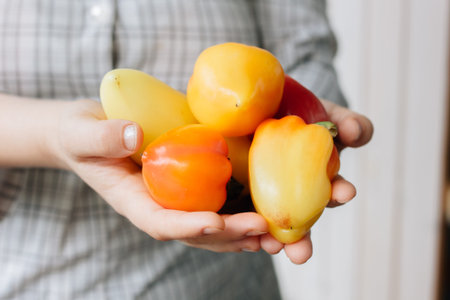 Woman holding hip of fresh bell peppers in hands.