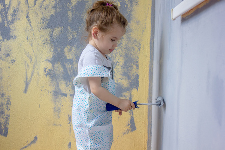 Little kid girl paints wall by paint rollerの写真素材