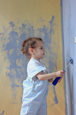 Little kid girl paints wall by paint rollerの写真素材