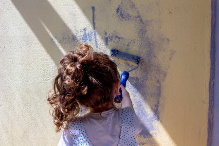 Little kid girl paints wall by paint rollerの写真素材