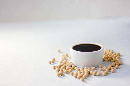 Soybean sauce surrounded by soy beans over white background.の写真素材